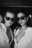 Black and white photo of two women wearing Ray Ban sunglasses and open white shirts, styled like a film still from a fashion-forward AI shoot
